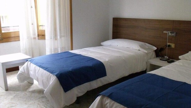 Una habitación de hotel con dos camas individuales, una mesita de noche y un ventanal con cortinas.