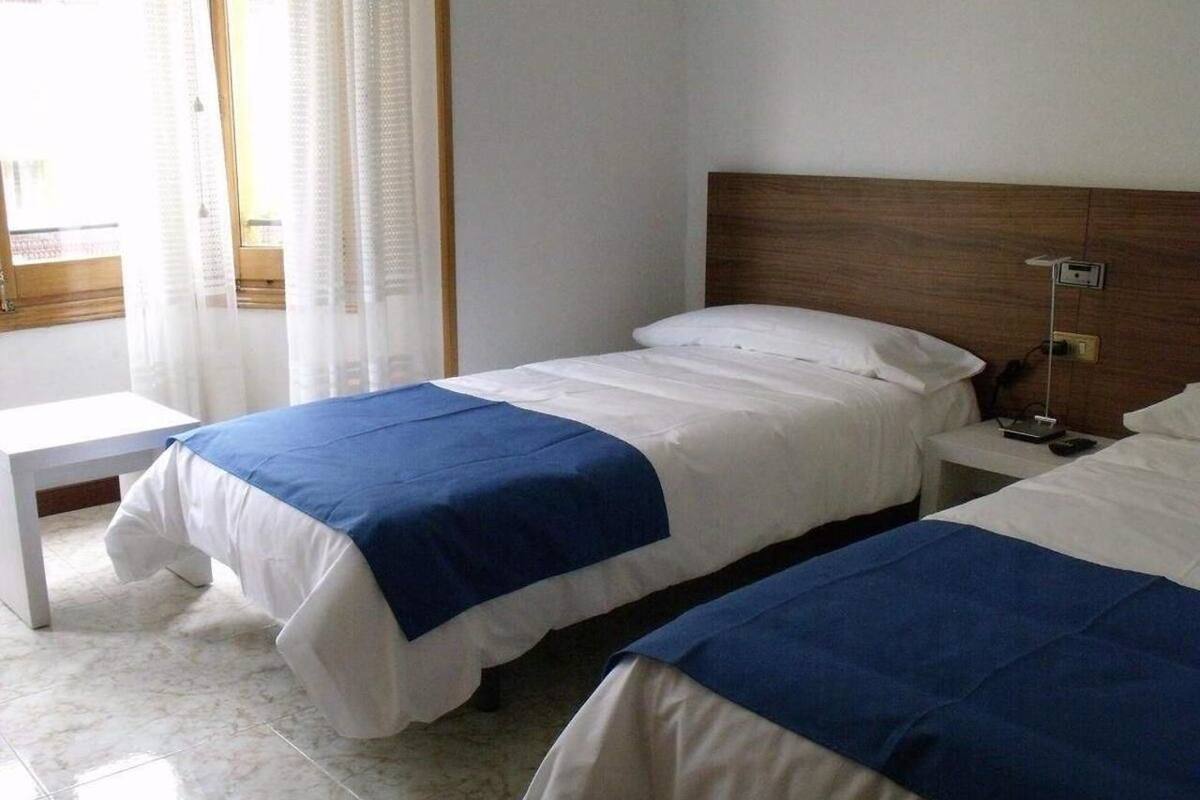 A hotel room with two single beds, a bedside table, and a window with curtains.