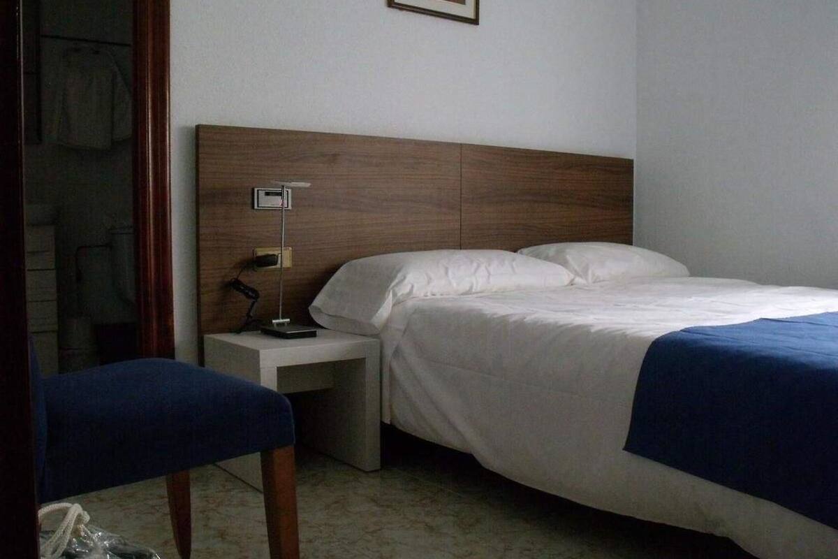 A hotel room with a bed, bedside table, lamp, and a chair.