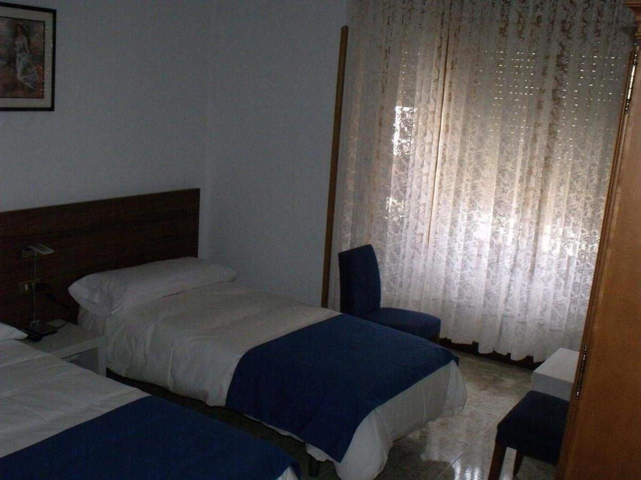 Una habitación de hotel con dos camas, una silla, un escritorio y una ventana con cortinas.