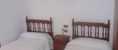 A bedroom with two single beds, a wooden nightstand with drawers, and a framed picture on the wall.