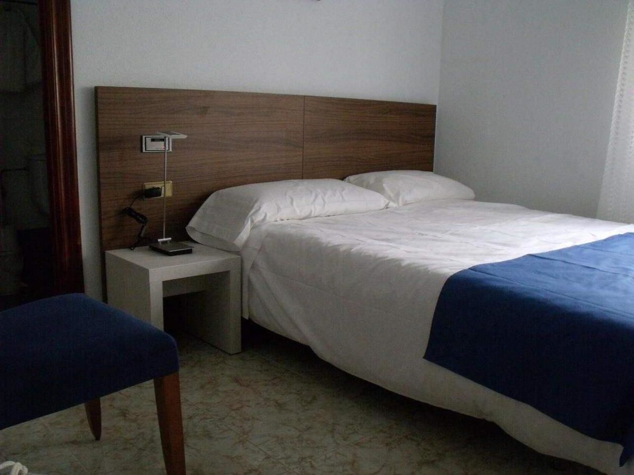 A single bed with a wooden headboard, a bedside table with a lamp, and a blue chair.