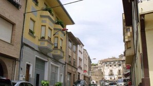 Una calle estrecha flanqueada por edificios de varios pisos, algunos con balcones y plantas.