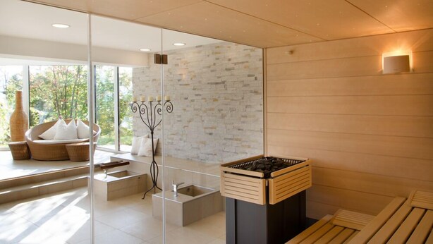 Un moderno spa con pared de piedra, sauna de madera, separador de vidrio y zona de estar con cojines.