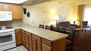A compact kitchen with a microwave, stove, and wooden cabinets. There is a dining area with a sofa, chairs, and a small table. - Pima Inn Suites at Talking Stick (Scottsdale)