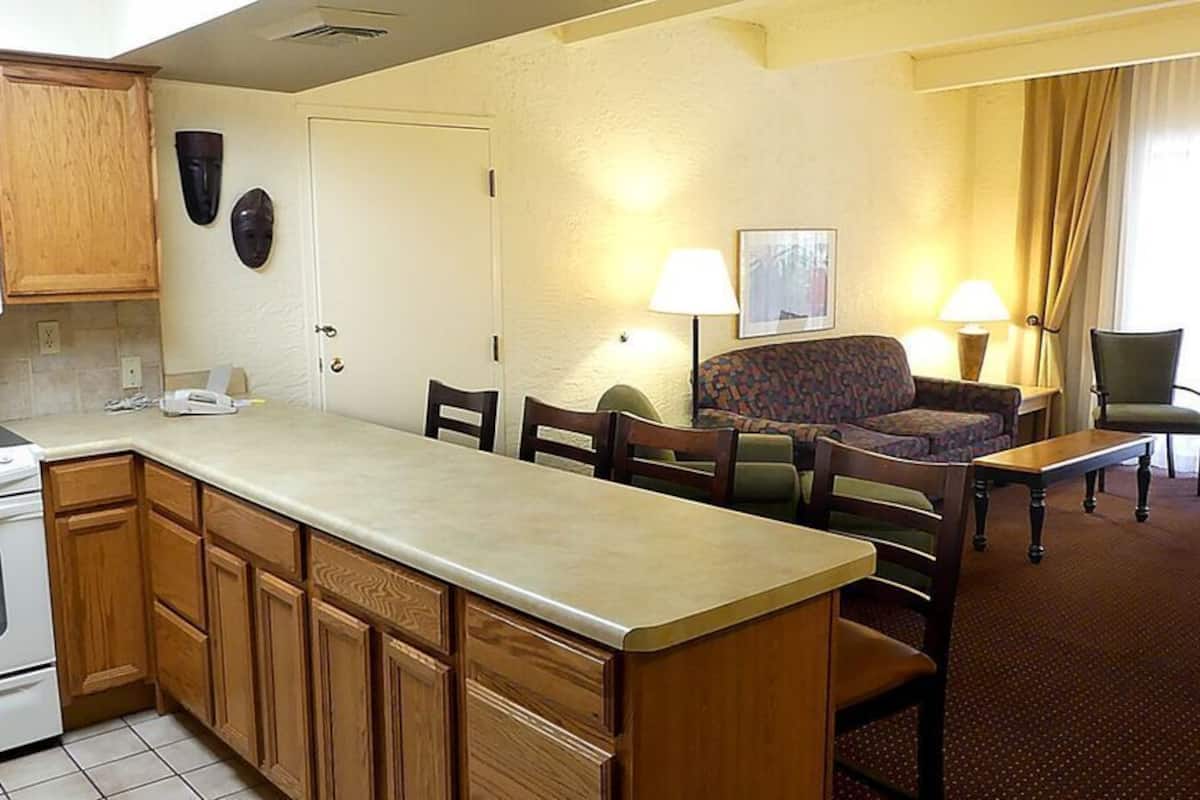 A compact kitchen with a microwave, stove, and wooden cabinets. There is a dining area with a sofa, chairs, and a small table.