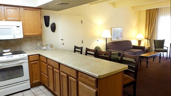 A compact kitchen with a microwave, stove, and wooden cabinets. There is a dining area with a sofa, chairs, and a small table.