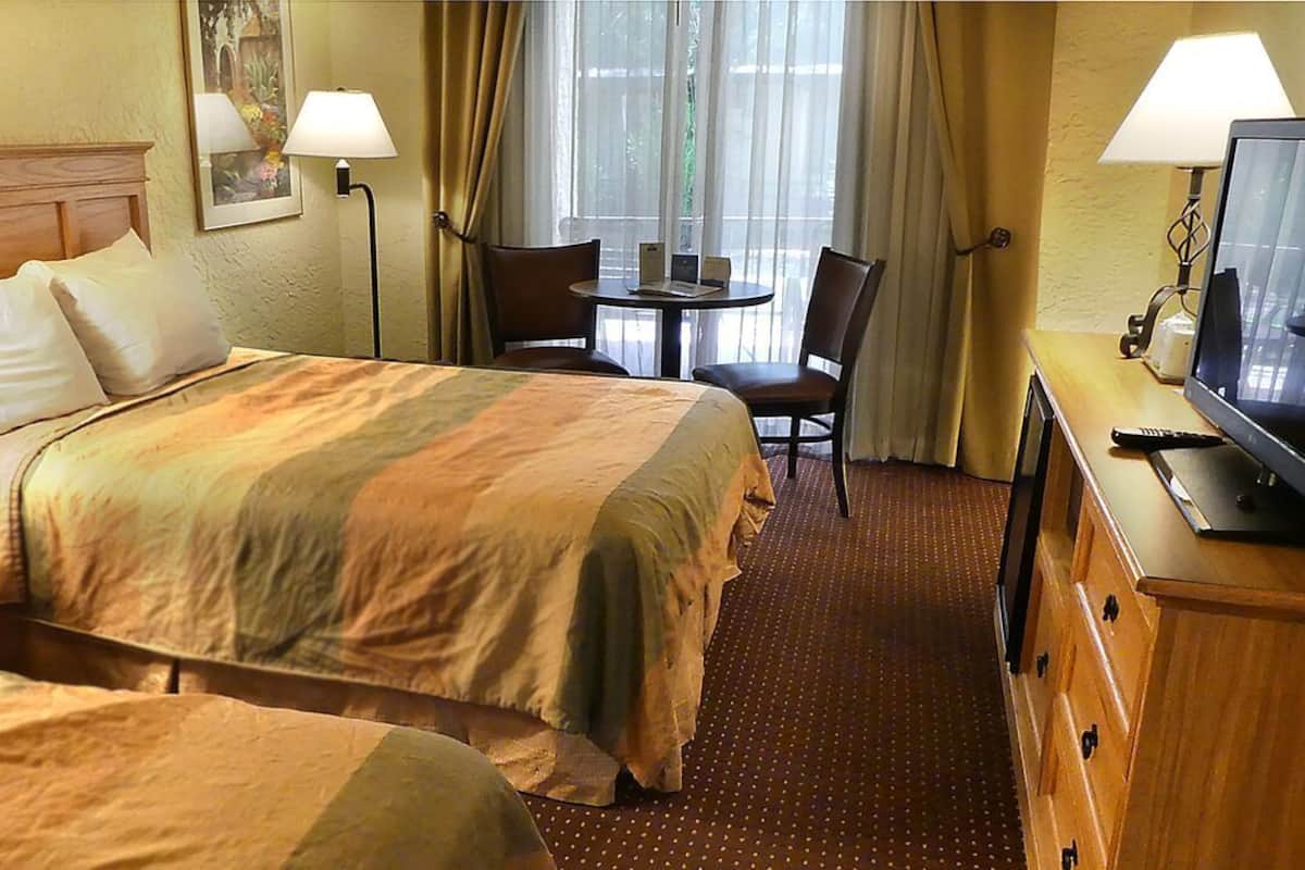 A hotel room with a bed, two chairs, a small table, a TV, and a lamp.