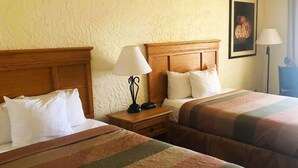 A hotel room with two beds, each with a wooden headboard and white bedding. There is a nightstand with a lamp and a radio between the beds. - Pima Inn Suites at Talking Stick (Scottsdale)