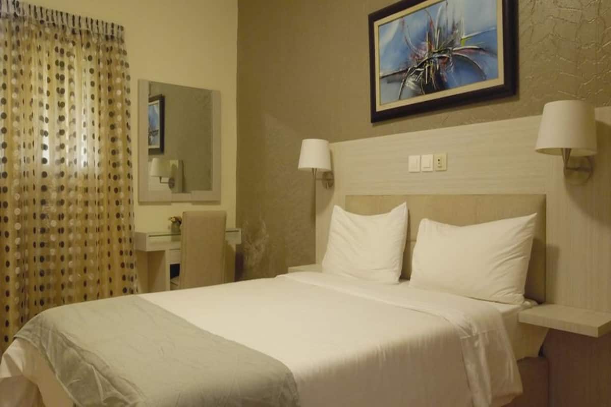 A hotel room with a bed, two bedside lamps, a mirror, and a painting on the wall.