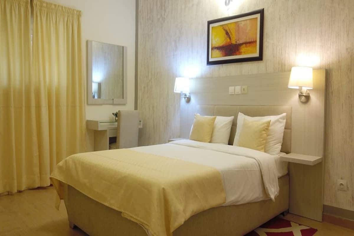 A hotel room with a bed, a nightstand, a lamp, a mirror, and a painting on the wall.