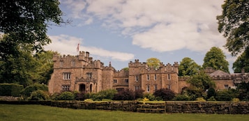 A large, historic stone building with multiple towers and turrets, surrounded by lush greenery and a stone wall.