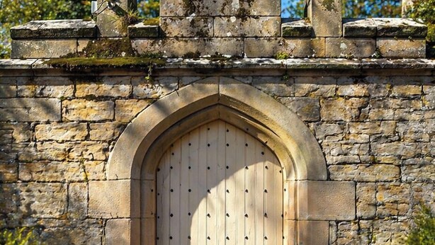 A stone archway leading to a wooden door with a lantern on the wall. - Otterburn Castle (Newcastle-upon-Tyne)