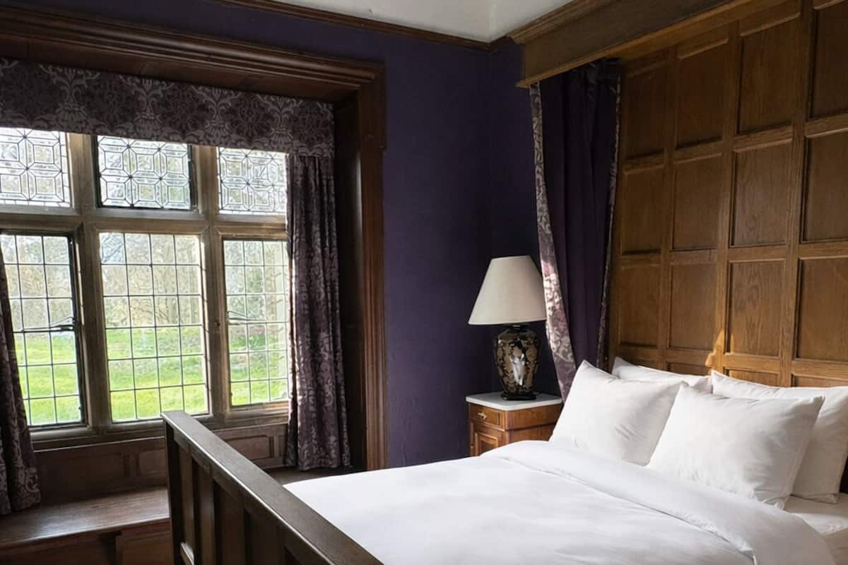 A bedroom with a large bed, a nightstand, a lamp, and a window with curtains.