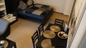 A compact room with a bed, a dining table with chairs, and a small shelf with folded clothes. - Apartment Auenviertel (Erfurt)