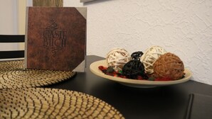 A table with a plate of decorative balls, a brown box labeled "Caste Buch," and woven placemats. - Apartment Auenviertel (Erfurt)