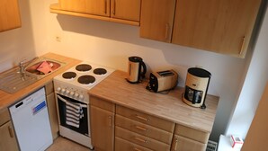 A compact kitchen with a dishwasher, stove, toaster, and coffee maker. - Apartment Auenviertel (Erfurt)