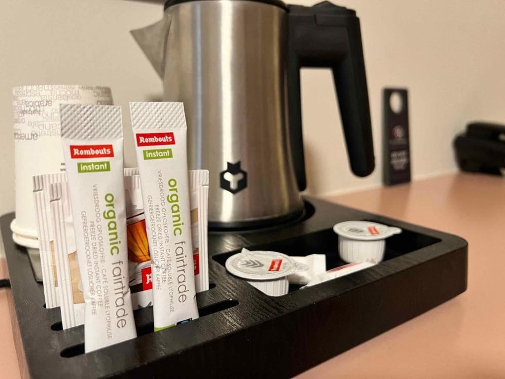 Une machine à café dotée d’un manche noir et d’un corps en acier inoxydable, accompagnée d’un support à dosettes contenant plusieurs dosettes.