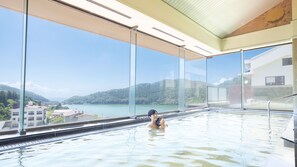A large indoor swimming pool with a view of a lake and mountains.