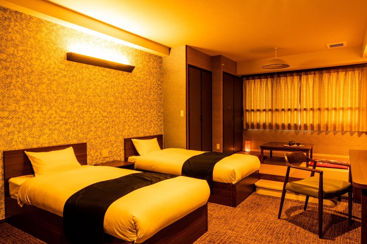Ein Hotelzimmer mit zwei Betten, einem kleinen Tisch, einem Stuhl und einem Schreibtisch.