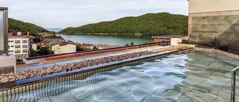 Piscina en la azotea con vistas a un lago y colinas.