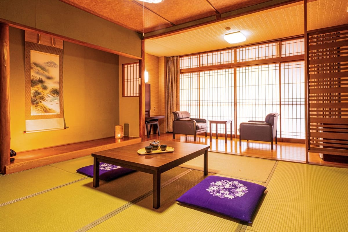 Ein traditioneller japanischer Raum mit Tatami-Böden, einem niedrigen Tisch mit Tee-Set und Schiebetüren mit Blick ins Freie.