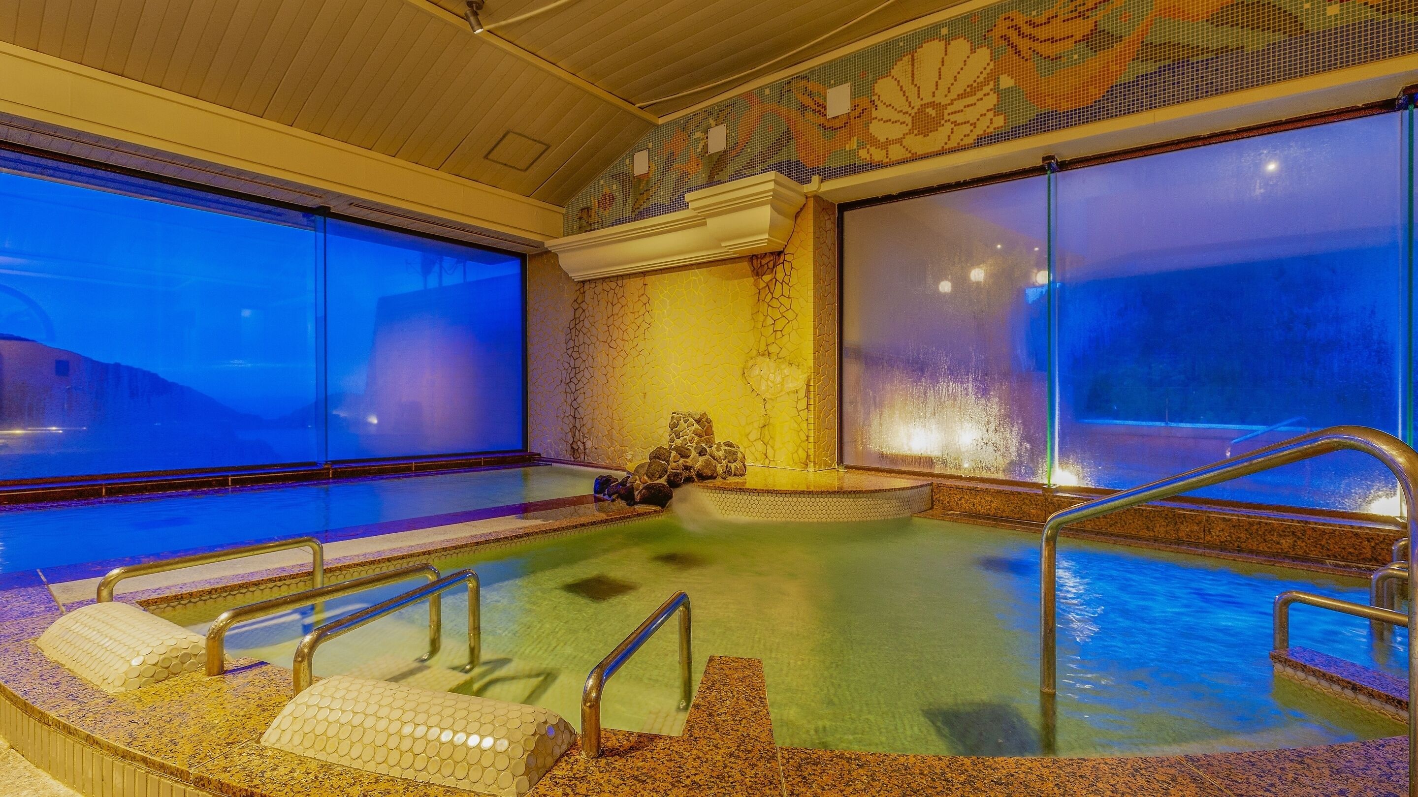 A hot tub with a view of the mountains, a mosaic wall, and a stone bench.