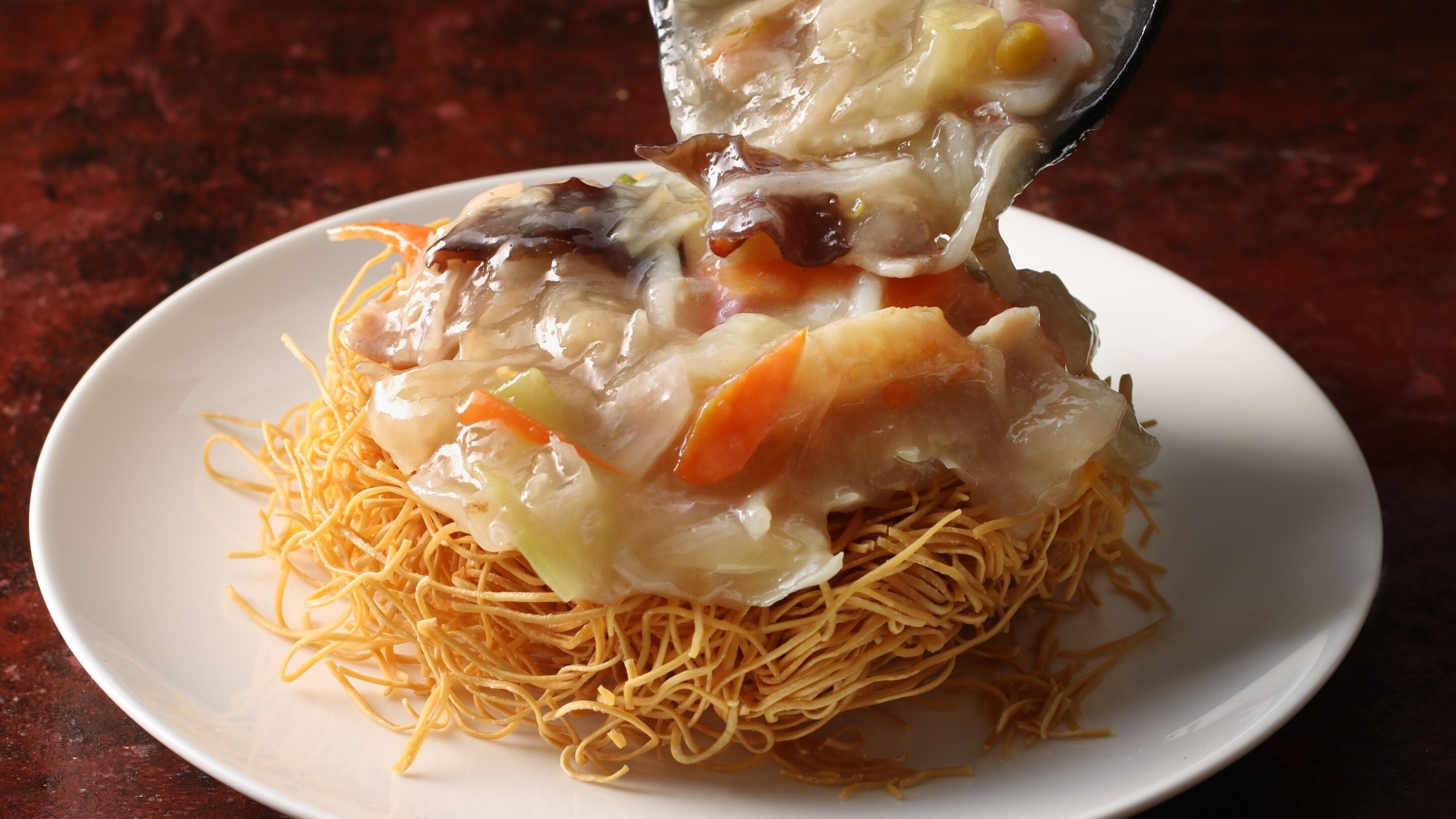 A plate of noodles topped with vegetables and shrimp, with a spoon lifting some of the food.