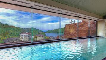 An indoor swimming pool with a view of a lake and mountains.