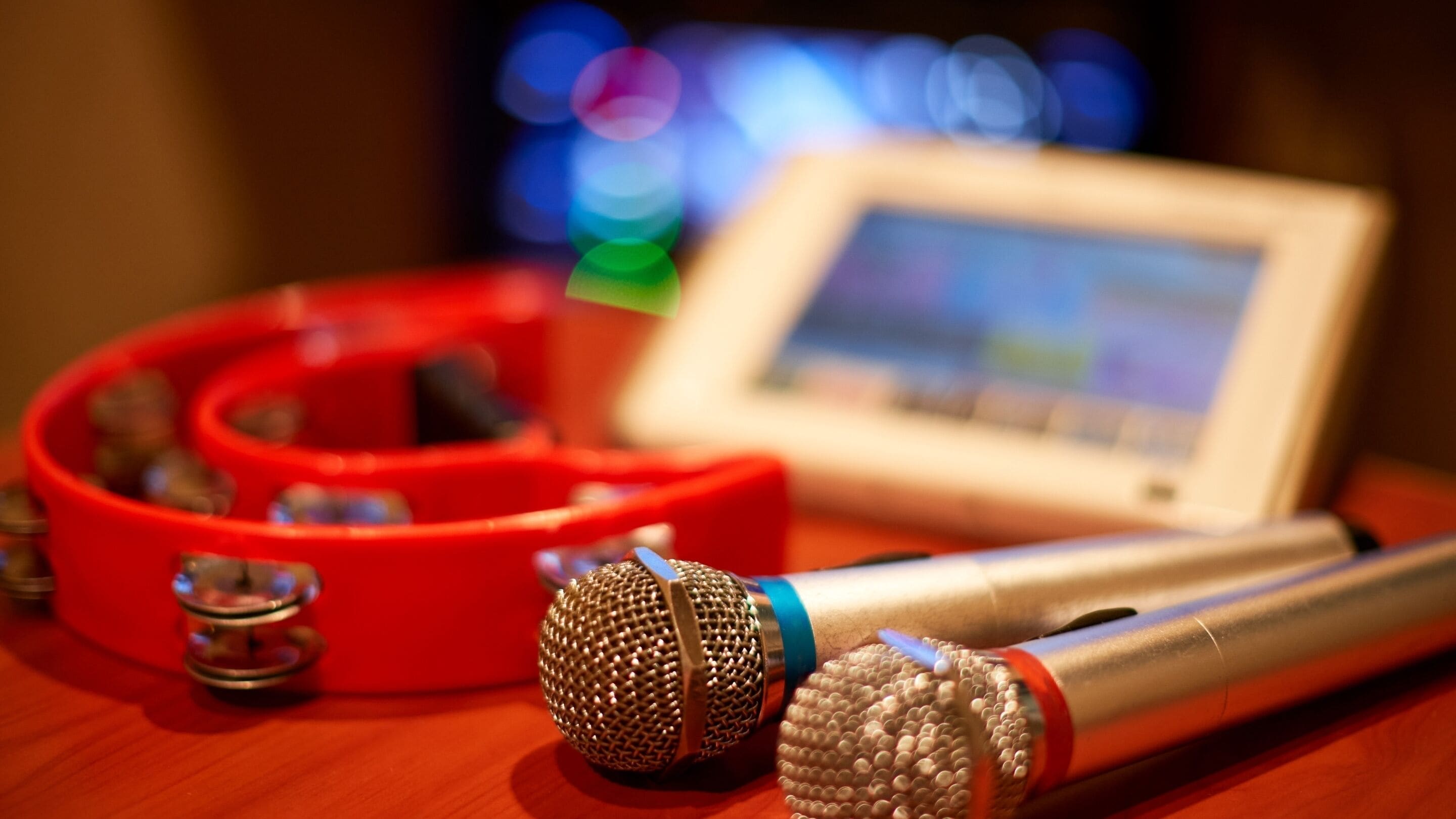 A microphone, a red speaker, and a tablet on a wooden surface.