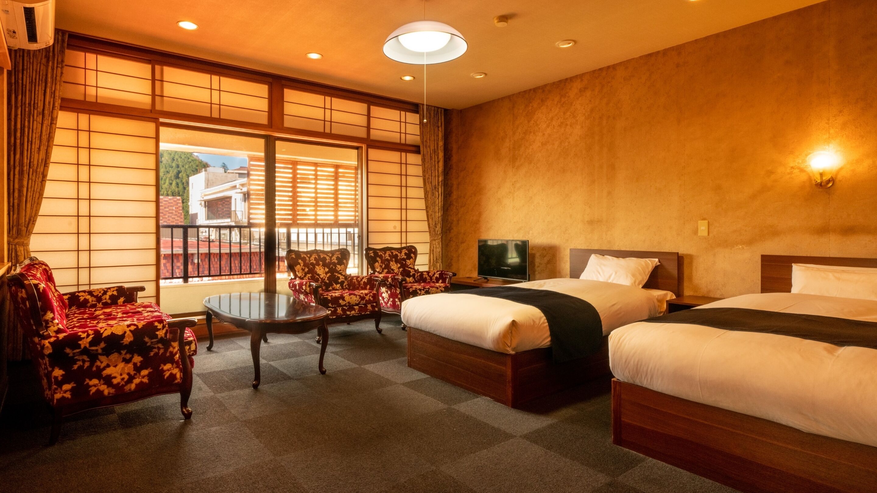A hotel room with two beds, a TV, a sofa, and a table.