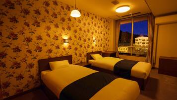 A hotel room with two beds, floral wallpaper, bedside lamps, a window with a view of buildings, and a ceiling light.