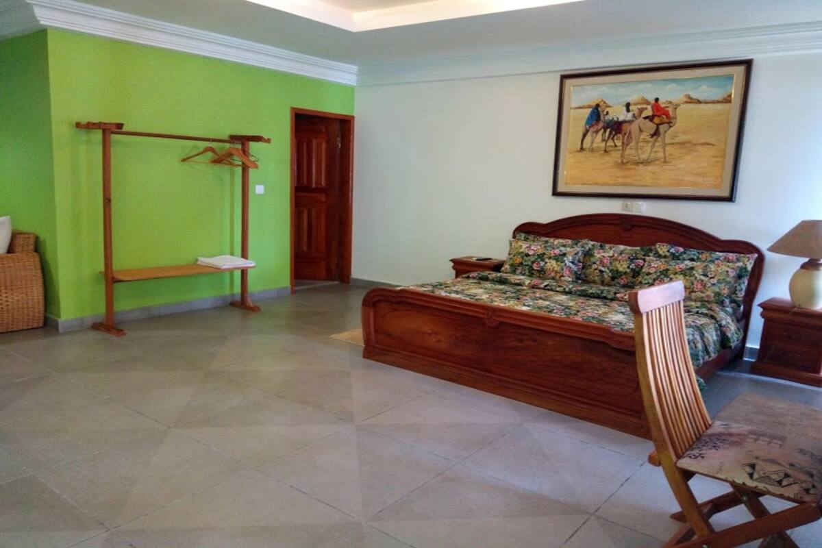 A bedroom with a wooden bed, a wooden chair, a wooden wardrobe, and a painting on the wall.