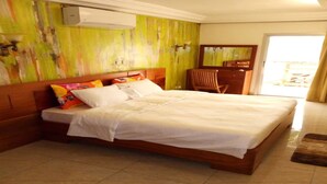 Habitación de hotel con una cama grande, cabecera de madera, un escritorio pequeño y una silla. Se ve una ventana con cortinas y vistas al exterior.