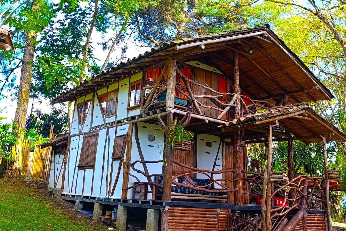 Una casa de madera rústica con techo de paja, rodeada de abundante vegetación y árboles.