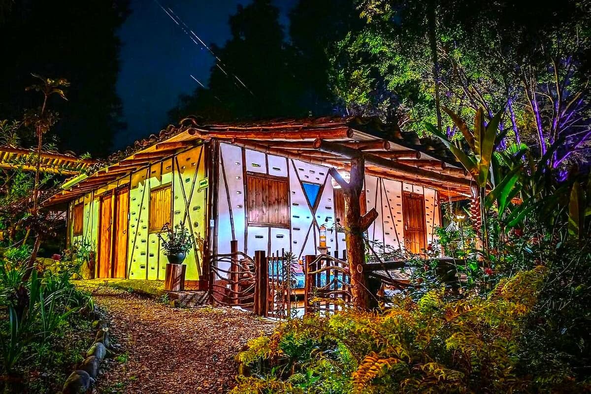 Una casa de madera rústica con techo de paja, rodeada de abundante follaje y un jardín bien cuidado.