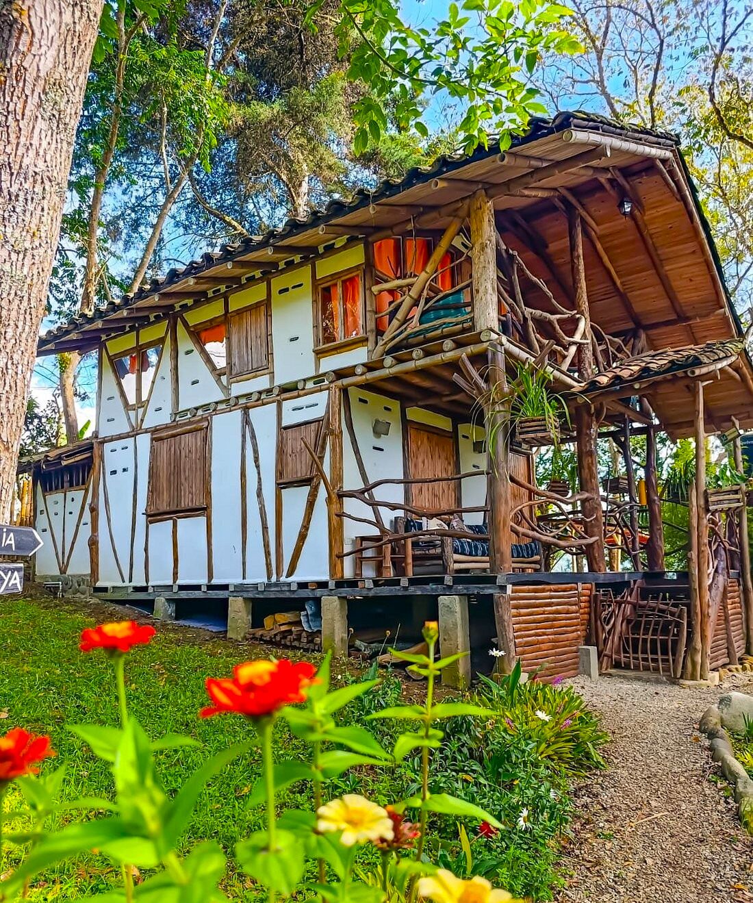 Une maison traditionnelle en bois, dotée d’un toit à pente, entourée d’une végétation luxuriante et de plantes en fleurs.