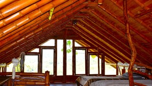 Ein Zimmer mit schrägen Wänden, Bambusbalken, zwei Betten und großen Fenstern.