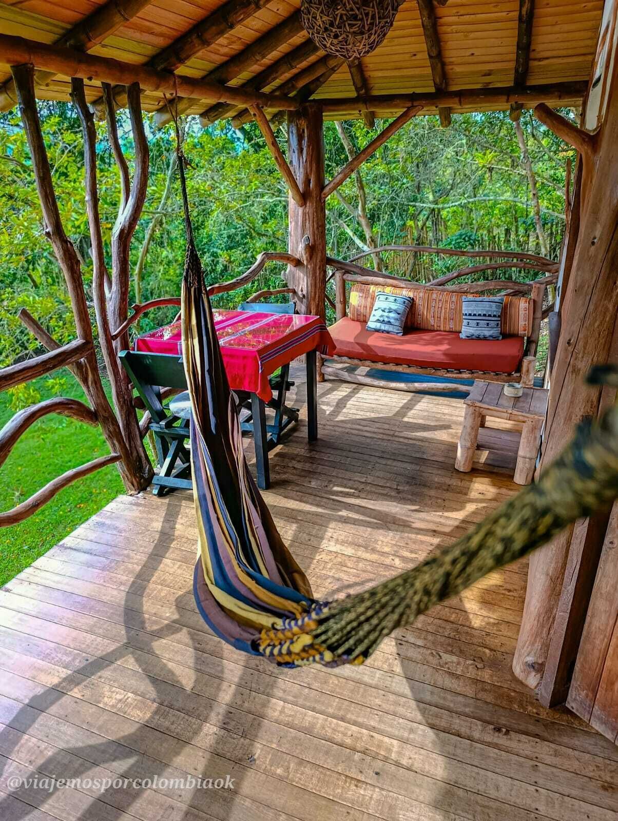 A wooden deck with a hammock, a red table, and a sofa with cushions.