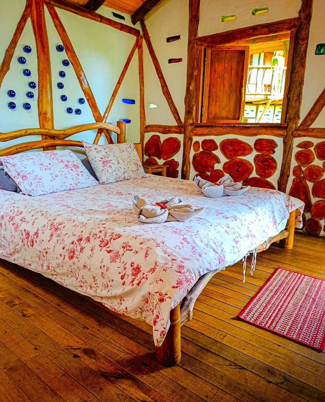 Un dormitorio acogedor con un cabecero de madera, ropa de cama floral y una decoración original en la pared con forma de corazones rojos.