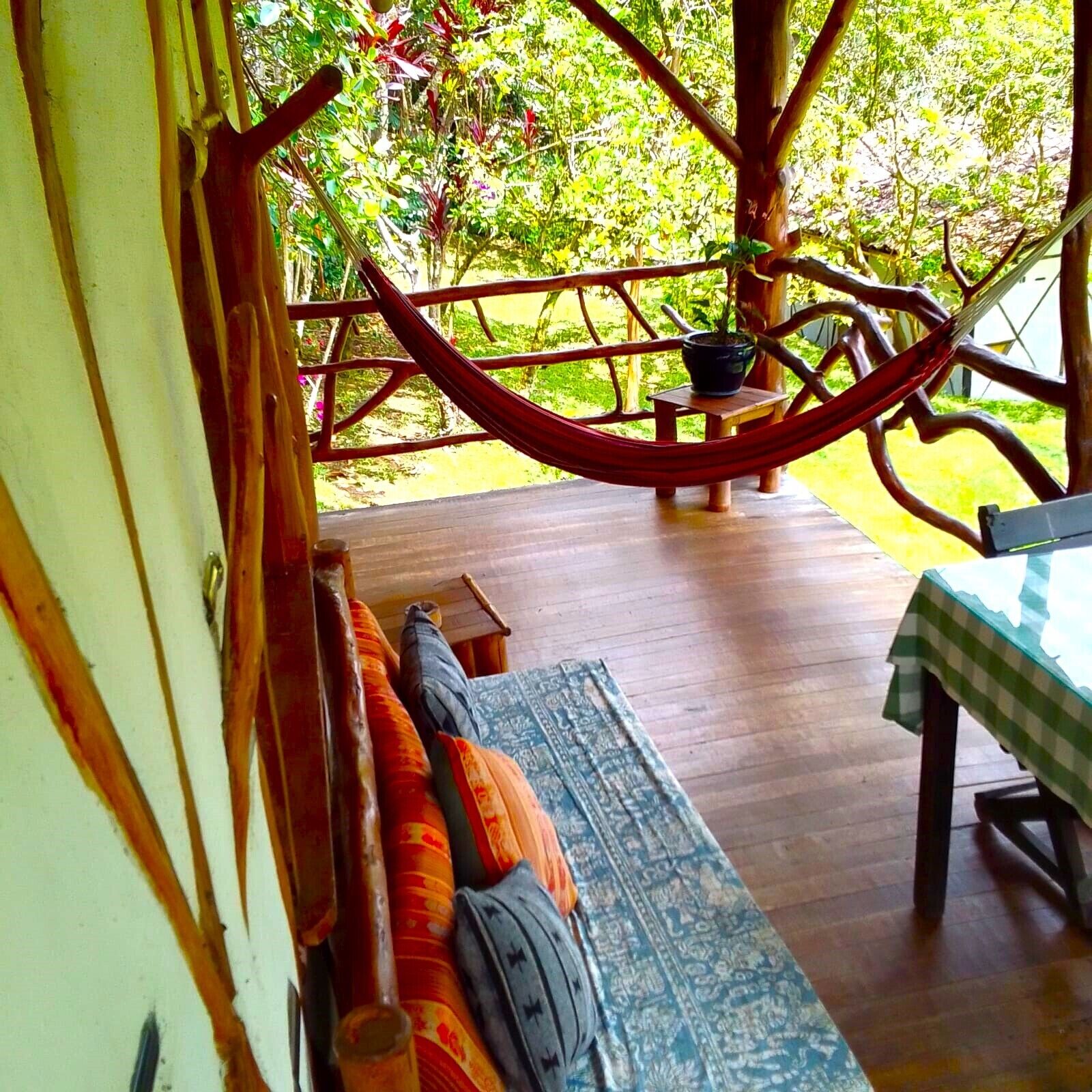 A wooden deck with a hammock, a table with a checkered tablecloth, and a patterned rug.