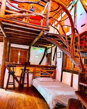 A rustic room with a loft bed, wooden beams, and a small desk.