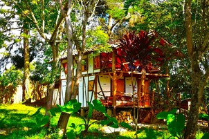 A treehouse with a wooden deck and a small porch, surrounded by lush greenery.