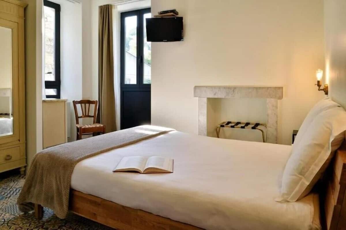 Un dormitorio con cama, una silla, chimenea y televisor en la pared.