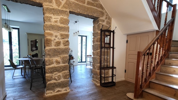 A spacious interior with a stone archway, wooden staircase, and a dining area with chairs and a table. - A Bella Scusa (Bastelica)