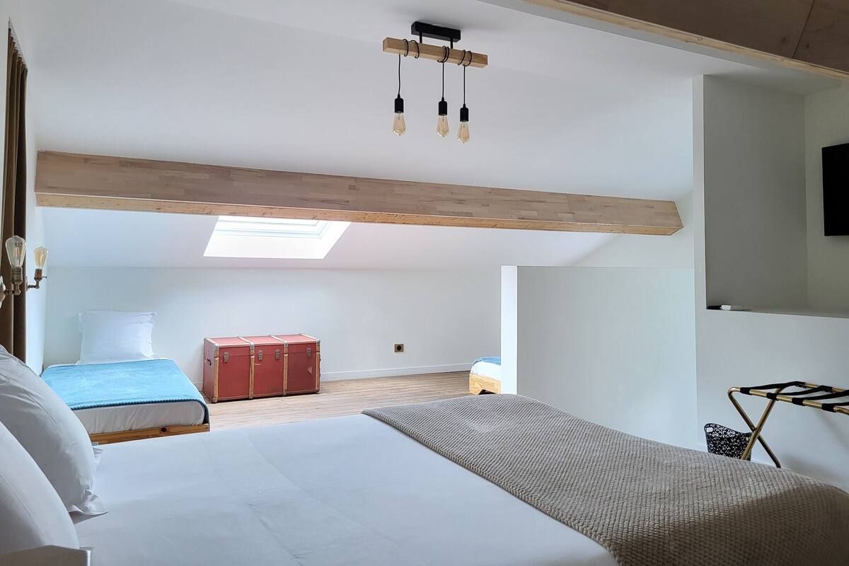 Un dormitorio con una cama grande, tragaluces, techo con vigas de madera y una maleta roja.