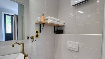 Un baño moderno con un lavabo blanco, grifo dorado y un inodoro. Hay un estante con toallas y una botella de jabón.