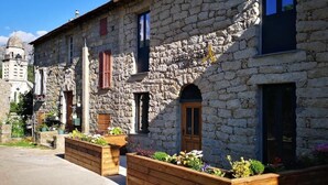 A stone building with wooden window shutters, a wooden door, and a small garden area with raised beds. - A Bella Scusa (Bastelica)