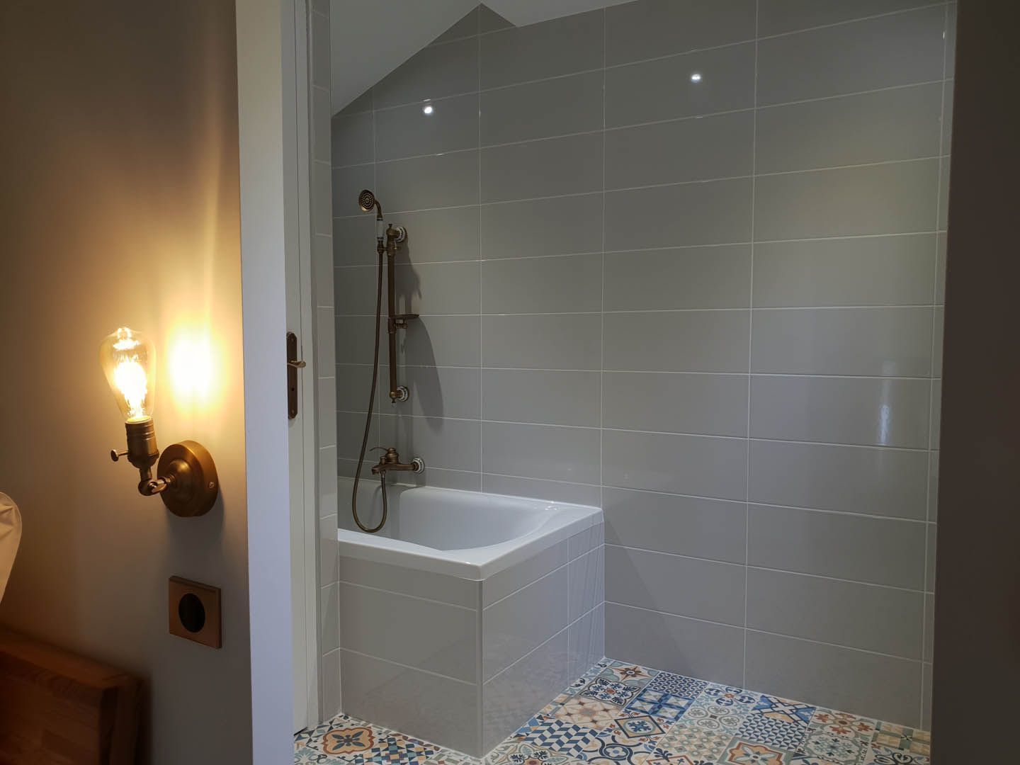 Un baño con una bañera blanca, ducha y piso de baldosas con un diseño geométrico.