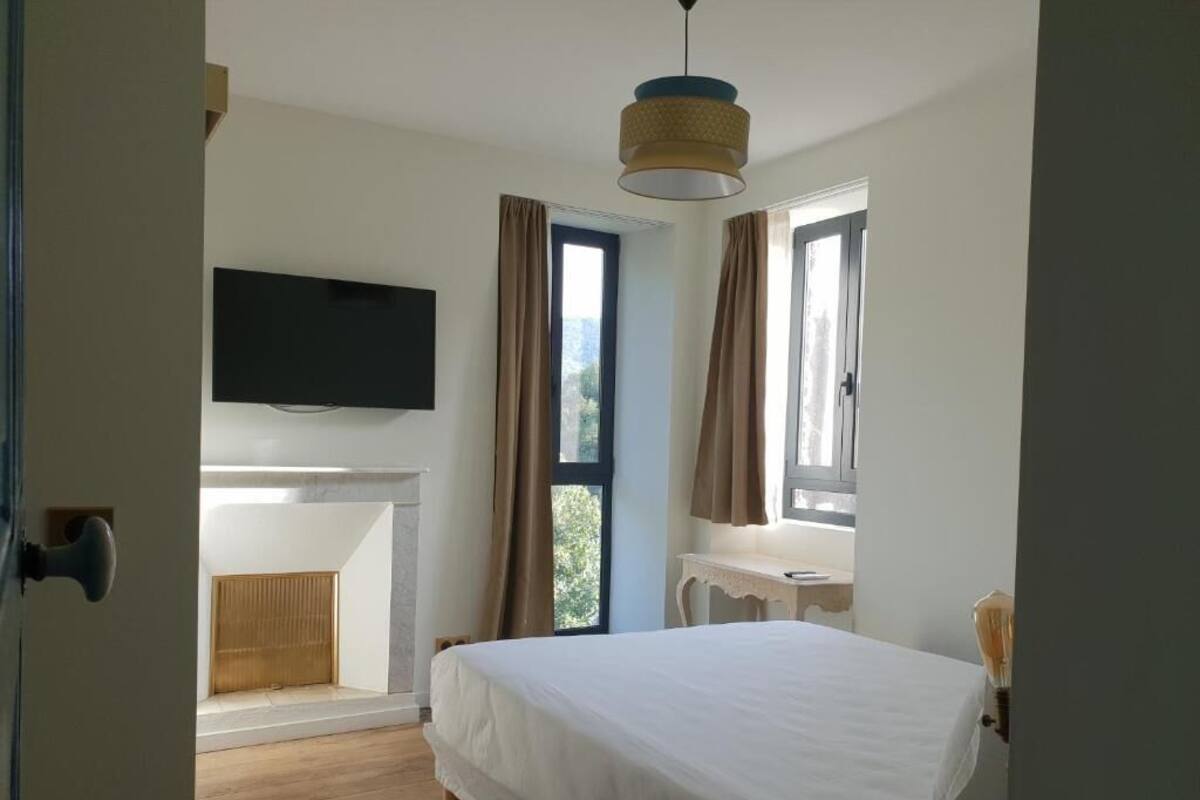 Un dormitorio con una cama, televisión montada en la pared, un escritorio y una ventana con cortinas.